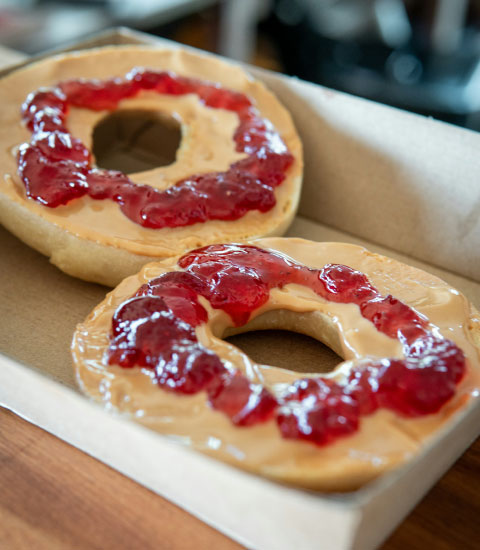 A sliced, toasted bagel with peanut butter and jam.